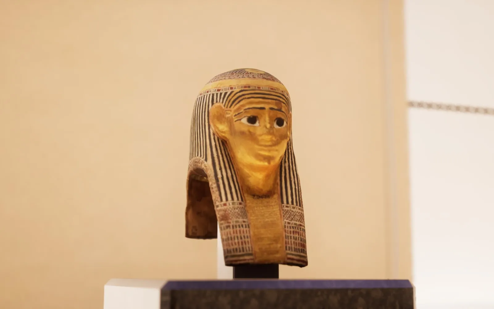 Máscara funeraria egipcia expuesta sobre una peana en una sala de museo